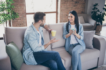 Portrait of positive loving married couple man woman have talk enjoy free time drink cappuccino cup sit couch in house indoors