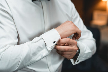Obraz na płótnie Canvas A man fastens cufflink on the white shirt. Close up of a man hand wearing a white shirt and cufflinks.