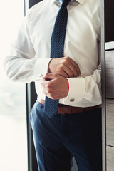 A man fastens cufflink on the white shirt. Close up of a man hand wearing a white shirt and...