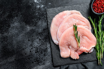 Turkey steaks with rosemary and pink pepper. Raw organic poultry meat. Black background. Top view. Copy space