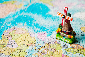 Tourist attractions and souvenir of Amsterdam windmill in background of the world map puzzle for travelers. Copy space