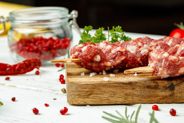 Raw lula kebab on skewers with spices on wooden board