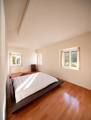 Interior of a minimal bedroom, with only one bed and a beam of light entering. The floor is made of wood and the bed is low, Japanese style. Nobody inside.