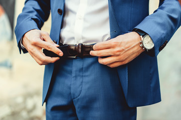 Groom in blue pants and a white shirt fastens his leather belt. grooms mourning. Wedding details.