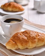 A cup of coffee  and croissant on wooden table.