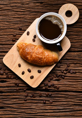 Top view a cup of coffee with coffee beans and croissant on wooden table.