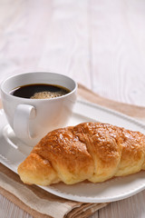 A cup of coffee  and croissant on wooden table