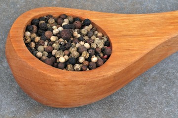 Cuillère en bois de poivre en grains en gros plan sur fond gris