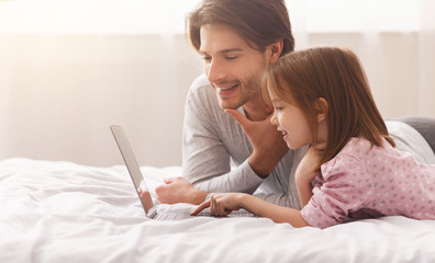 Little girl learning how to use laptop, young father helping