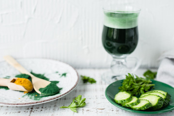 The concept of detox flying and health. Spirulina and turmeric powder. cucumber, parsley, aloe vera and green smoothie on a white wooden background