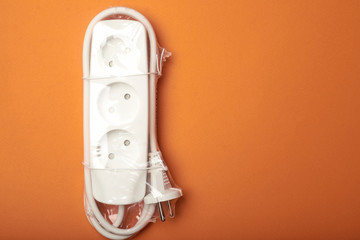 Electric extension cord in packaging on an orange background.
