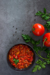 Traditional mexican salsa sauce, fresh tomatoes, parsley, pepper on black stone table.Homemade tomato sauce with red bell pepper, onion, olive oil, garlic, fresh basil. Top view, vertical, copy space