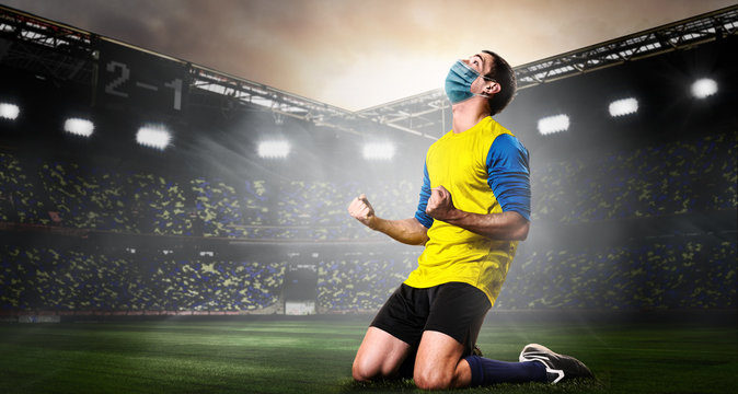 Soccer Or Football Player Wearing Mask. Team Sports Player In Medical Mask Emotionnally Kneeling On Stadium During Coronavirus Outbreak.