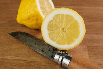 Eine frisch aufgeschnittene gelbe Zitrone mit einem rustikalen Messer auf einem Holz-Hintergrund
