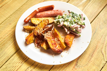Fried crispy potato with cheese, sausages and salad on a white plate on a wooden background.