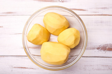 Peeled potato tubers in a plate on a light wooden background. Preparing potatoes for cooking.