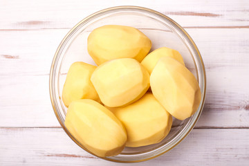 Peeled potato tubers in a plate on a light wooden background. Preparing potatoes for cooking.