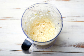 Finely chopped onions in a blender bowl on a light wooden background.
