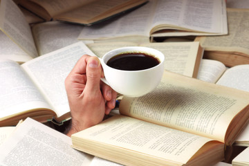 Naklejka premium Man bombarded with open books with a cup of coffee in hand. A man buried in literature.