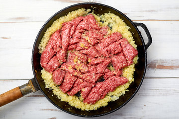 minced meat and onions in a pan on a light wooden background. Cooking toppings.