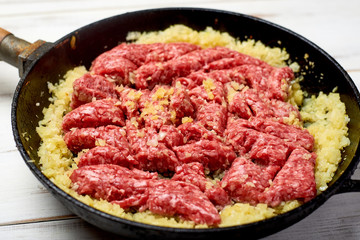 minced meat and onions in a pan on a light wooden background. Cooking toppings.
