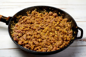 Grilled minced meat with onions, spices and cream in a pan on a light wooden background. Cooking toppings.