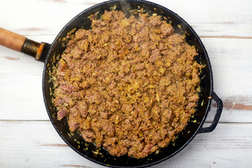 Grilled minced meat with onions, spices and cream in a pan on a light wooden background. Cooking toppings.