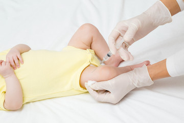 Doctor hands in rubber protective gloves holding syringe. Infant receiving vaccine in leg. Visit to pediatrician at hospital. Two month old baby. Close up.