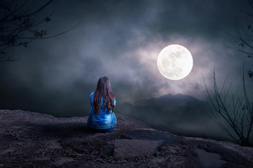 Young Woman sitting alone on the mountain to watch the full moon at night, nature background, Back view