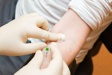 Doctor hand in rubber protective glove putting white cotton wool after took blood from vein of young man arm. Visit to physician at office. Close up.