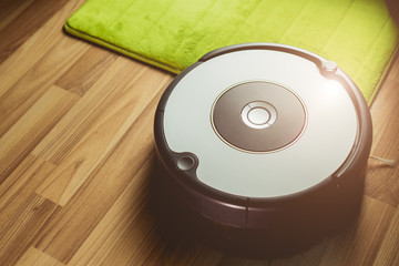 Robot vacuum cleaner cleaning on wooden floor with carpet on the apartment home ground sunny light.