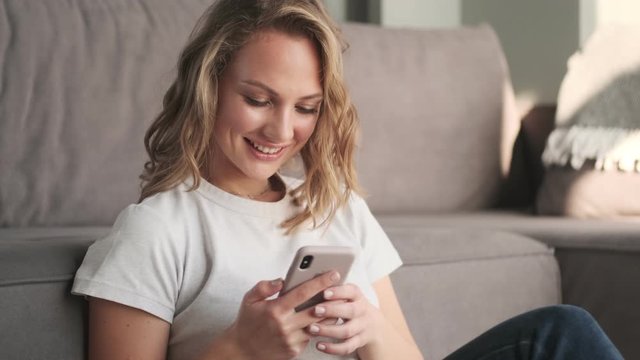 Young optimistic woman indoors at home using mobile phone