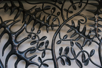 A metal grill in the form of a tree branch with black leaves on a light gray background. Original background for copy space.