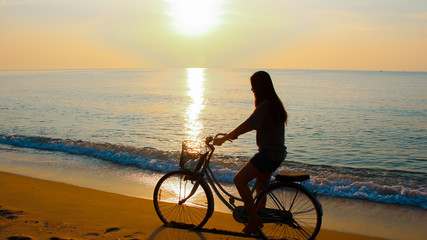 Fototapeta na wymiar Silhouette of a woman riding a bike and sunrise at the beach