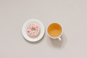 Obraz na płótnie Canvas The minimalist banner coffee break. Green tea in a white porcelain Cup and pink donut on a white plate on a beige background. Morning dessert