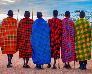 Group of Maasai tribesmen from East Africa with spears and colourful traditional shuka cloth dress (African blanket) looking away from the camera. - obrazy, fototapety, plakaty