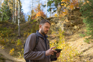 mężczyzna z brodą w lesie, na szlaku turystycznym, jesienią,  patrzy  na ekran telefonu  - obrazy, fototapety, plakaty