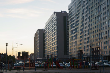Fototapeta premium Evening view of cityscape, car-filled courtyard in front of high-rise buildings, children playground.
