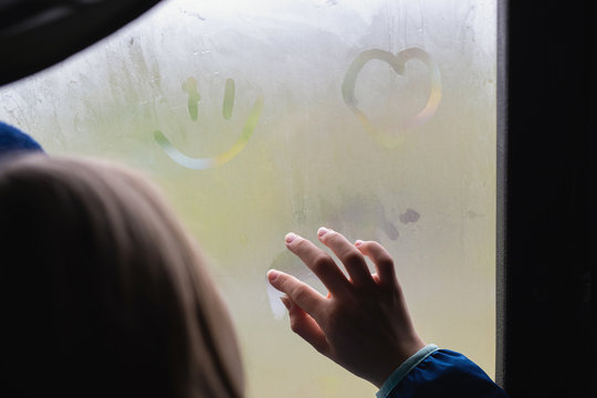 girl or young women hand draws on misted, foggy window. finger on wet glass draws the heart, window and rain.