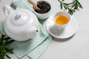 Cup with organic tea and teapot on white stone table background.