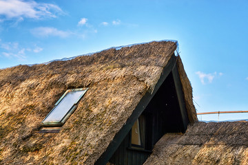 Detail of an old thatched roof under a blue sky.