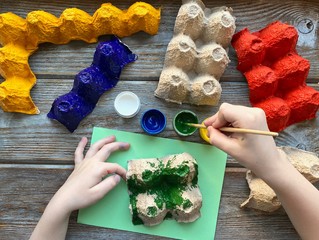 Children's hands paint the egg box with different colors