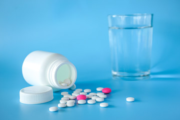 Close up of teblets pills with pill bottle and a glass of water on blue background 