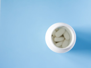 Pills of vitamin in the opened white plastic container on soft blue background.