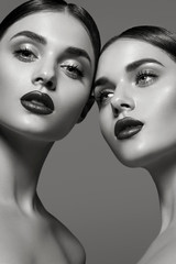 Two beautiful young girls with collected dark hair with perfect skin and juicy lips in the studio.