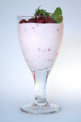 Yogurt with raspberries in a clear glass decorated with mint on a white background