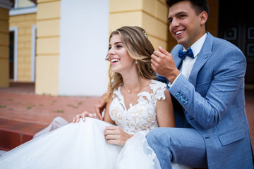 Naklejka premium Young stylish guy in the costume of the groom and the bride beautiful girl in a white dress with a train walk in the park on their wedding day