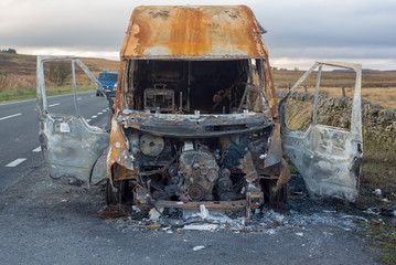 The burned out wreckage of an old van in a road layby 