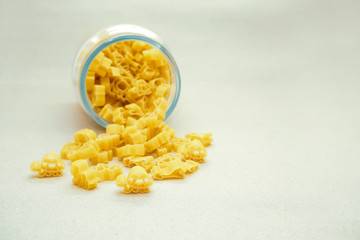 Baby eco-pasta from durum wheat in the form of animals falls out of a glass jar on a light background. Yellow pasta in the form of animals on a beige background. Baby food.