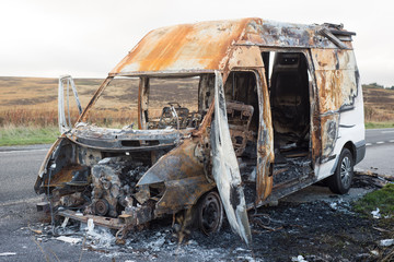 The burned out wreckage of an old van in a road layby 